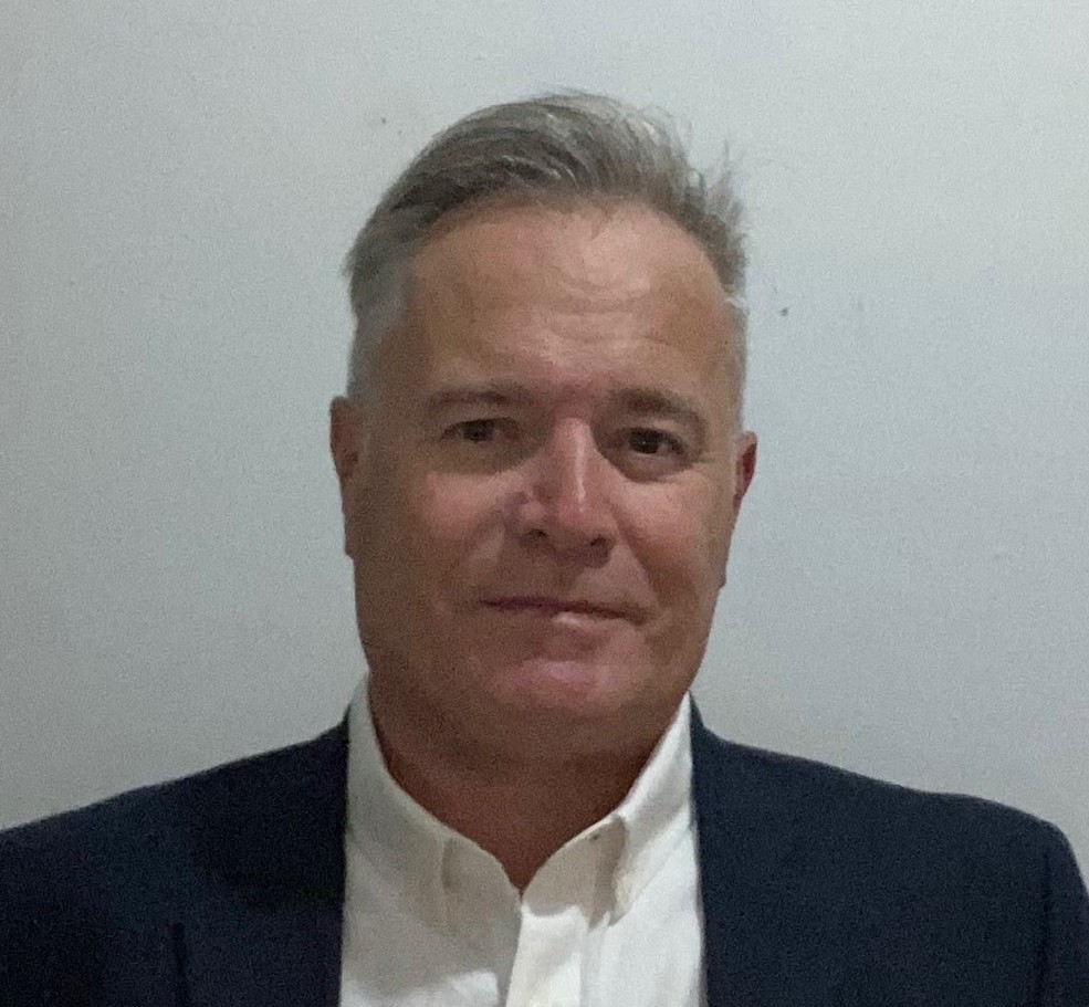 A photograph of Michael Fawley. He is a white man with grey hair and brown eyes. He is wearing a suit and white buttondown shirt, with a slight smile on his face.